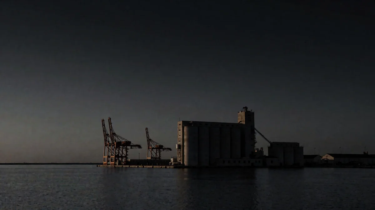 Un puerto con silos y grúas en silueta sobre el agua quieta al anochecer