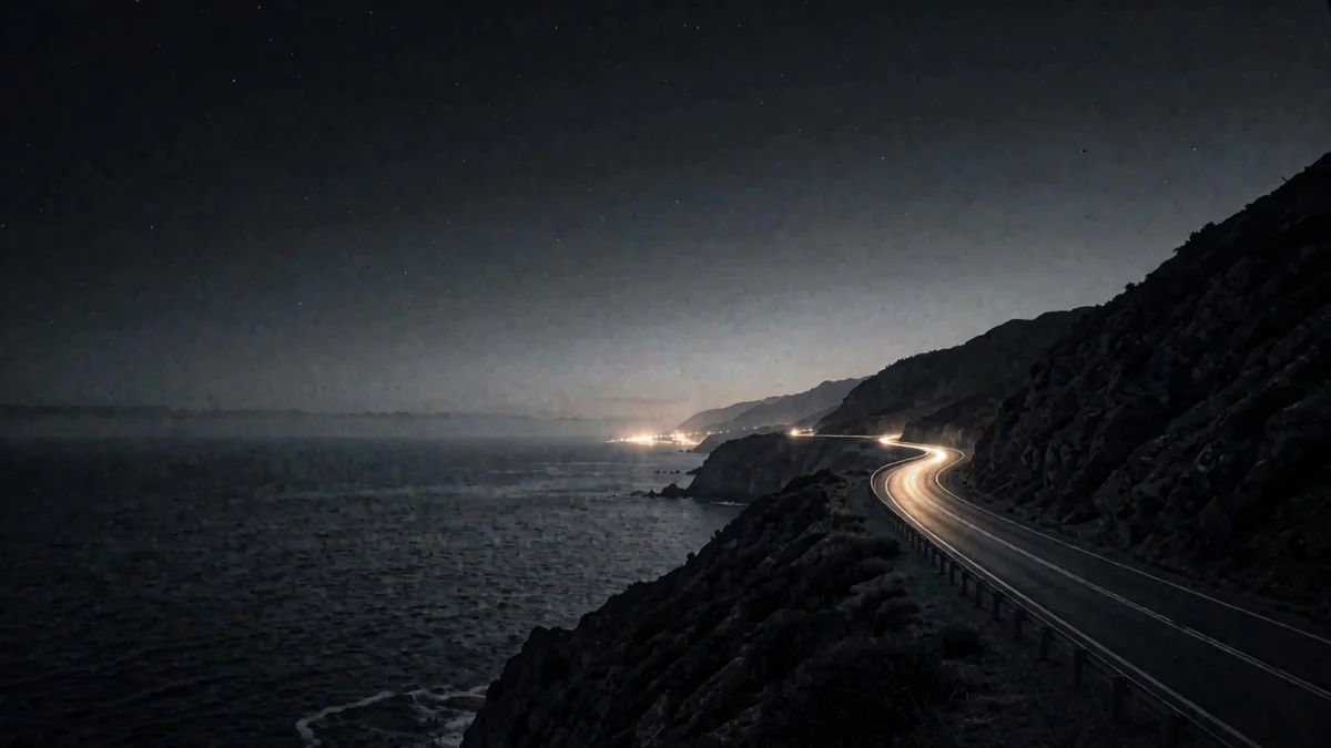 La carretera escénica sobre el Pacífico entre acantilados en hora azul con una luz cálida lejana
