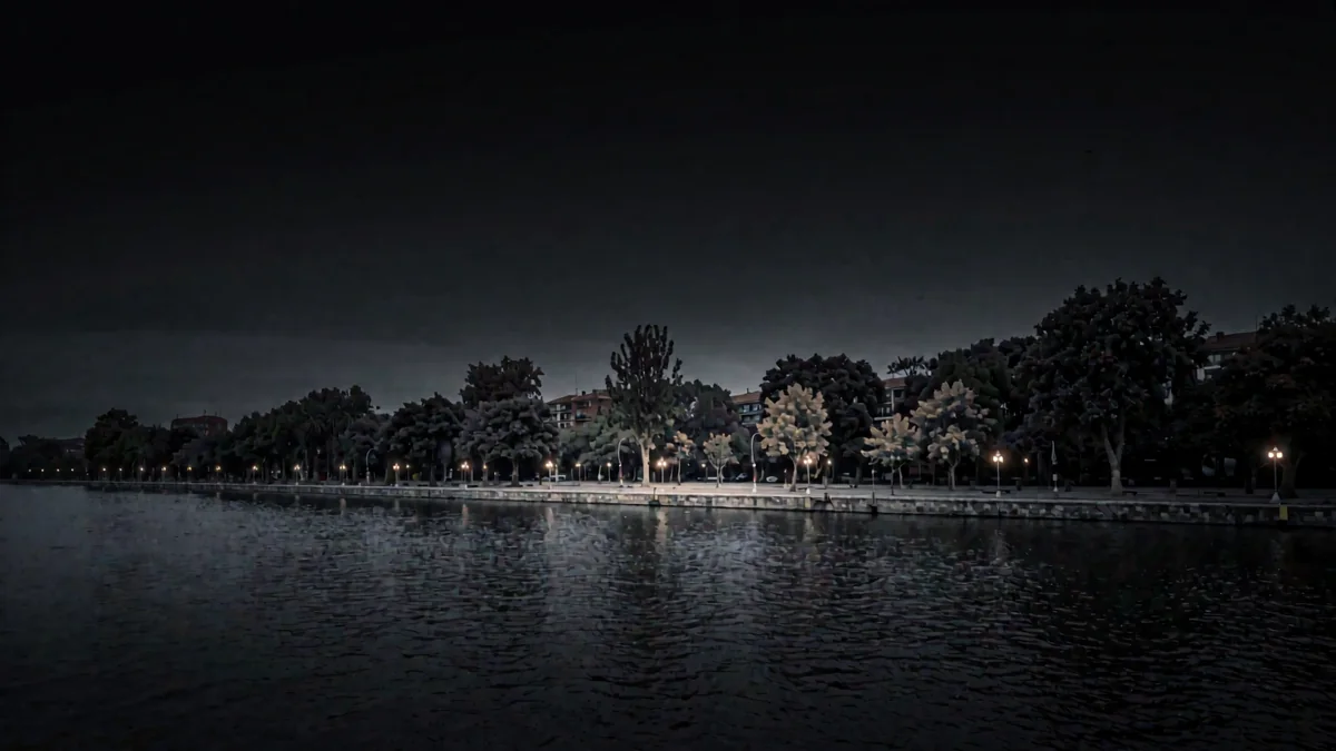 La costanera de un río ancho con árboles y faroles cálidos en hora azul